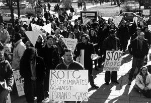 A group of protestors gather outdoors holding signs against ROTC’s anti-gay policy. Signs read “ROTC discriminates against Lesbians and Gays” and “Stop ROTC discrimination.”