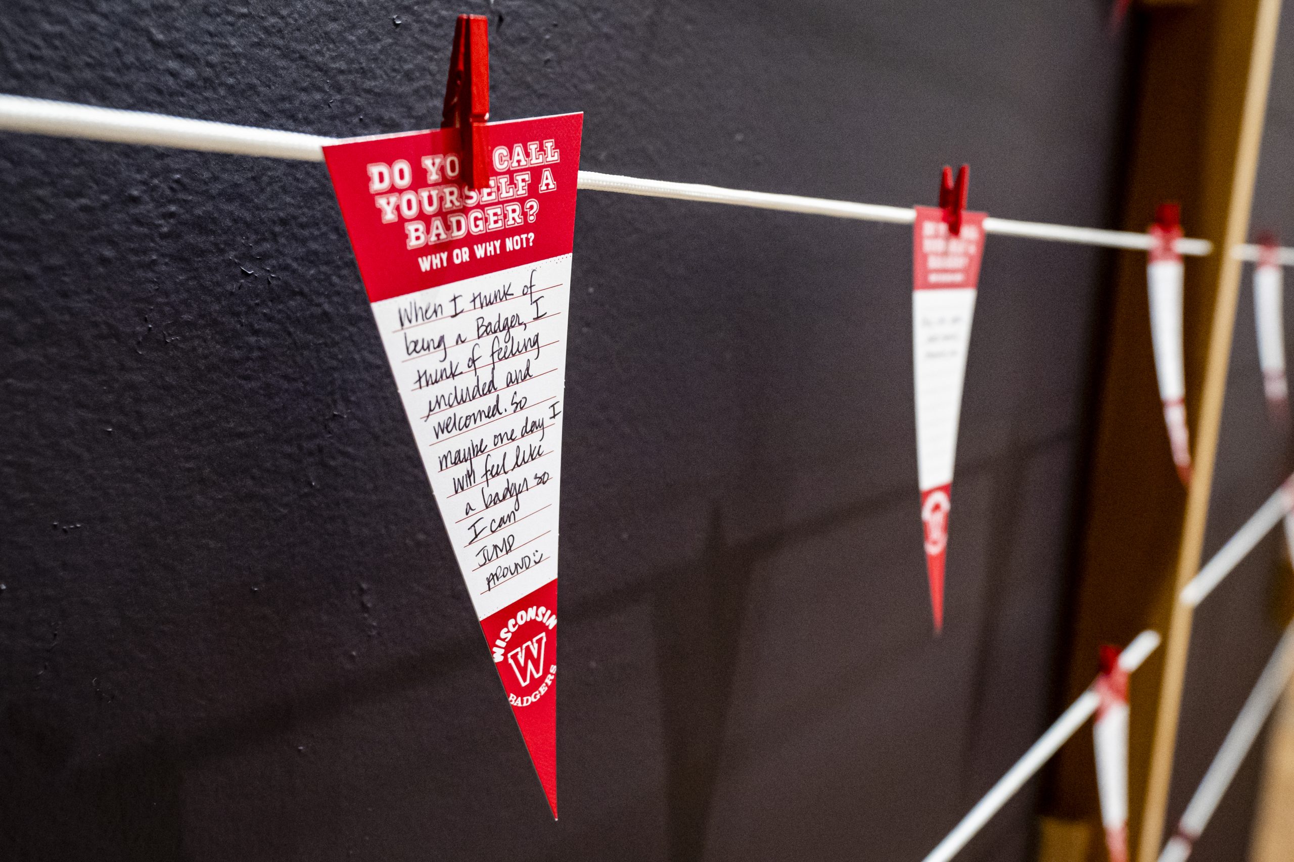 A red and white paper pennant with a handwritten note pinned to a white string, in front of a black wall. 